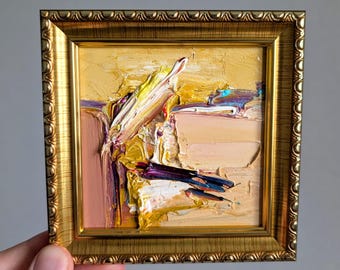 May include: A small square oil painting featuring thick impasto brushstrokes in shades of yellow, gold, peach, and deep purple. The artwork is encased in a decorative, ornate metallic gold frame with a scalloped edge detail.