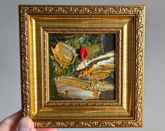 Könnte beinhalten: Ein kleines quadratisches Ölgemälde mit dicken, strukturierten Impasto-Pinselstrichen in Dunkelgrün, Gold, Weiß und einem einzelnen hellroten Akzent. Das Kunstwerk ist in einem verzierten, goldfarbenen Rahmen mit wiederkehrendem Schnörkelmuster.
