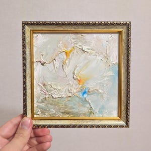 Impresionante pintura abstracta texturizada de 6 x 6 pulgadas con trazos gruesos de empasto en tonos suaves de blanco, dorado, azul y gris con un marco dorado listo para colgar