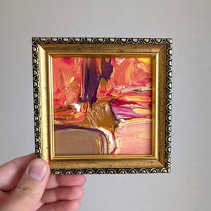 Pintura abstracta vibrante con empasto enmarcada en oro, tonos cálidos y ricos de rosa, naranja, rojo, morado y marrón, pinceladas con texturas audaces, sensación lujosa
