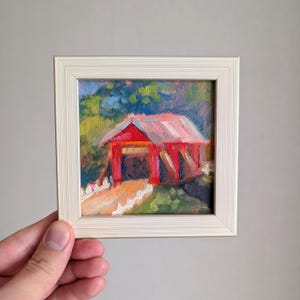 Pintura al óleo enmarcada pequeña, puente cubierto de rojo, árboles frondosos, camino terroso, tonos rústicos cálidos, sensación acogedora, cocina de granja ideal, Vermont