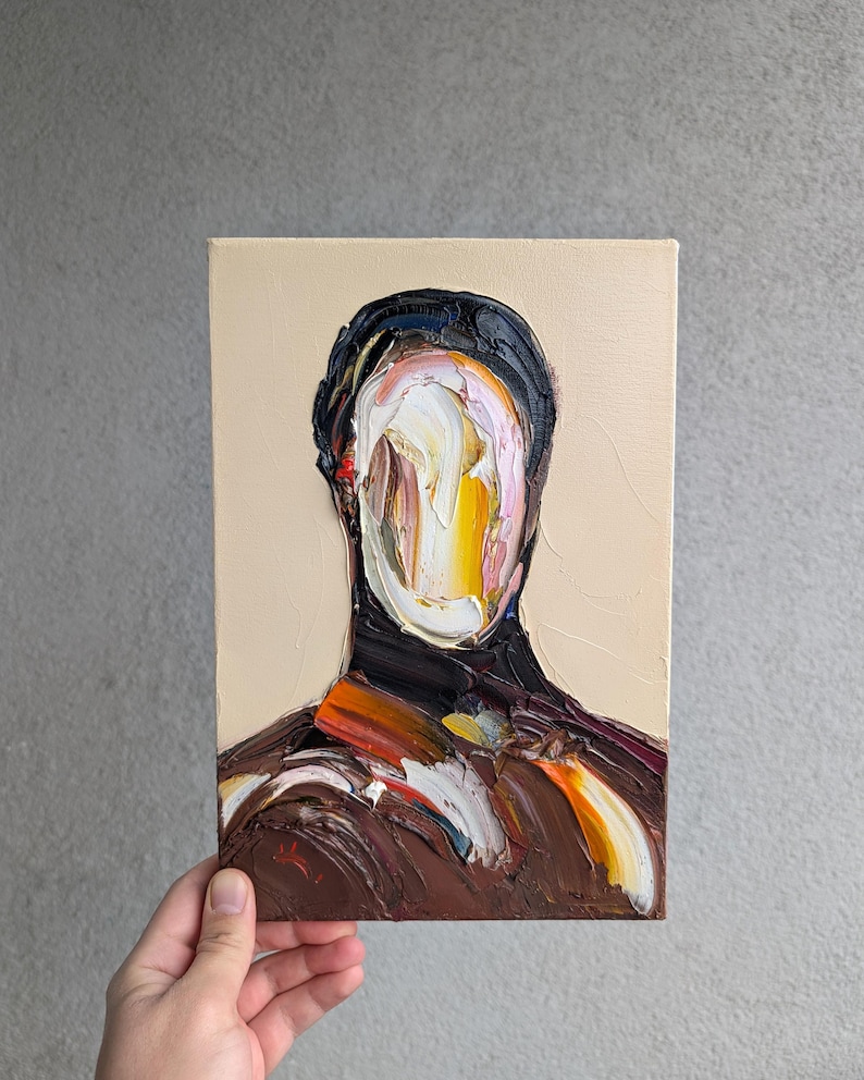 Puede incluir: Pintura al &oacute;leo sobre lienzo que representa una figura sin rostro. La obra presenta gruesas pinceladas en tonos marr&oacute;n, negro, naranja y blanco sobre un fondo beige. La pintura est&aacute; sostenida por una mano.