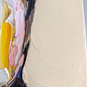 Puede incluir: Primer plano de una pintura al &oacute;leo abstracta que presenta un retrato con gruesas pinceladas. La obra de arte utiliza una paleta de amarillo, rosa, negro y blanco, con un fondo beige neutro. La pintura texturizada crea un efecto tridimensional.