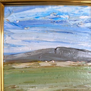 May include: Impasto oil painting of a landscape with a mountain, sky, and field. The sky is a mix of blues and white, the mountain is gray, and the field is green and tan. The painting is in a gold frame.