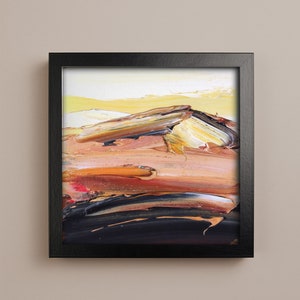 May include: Abstract oil painting in a black frame. The artwork features textured brushstrokes in shades of yellow, orange, brown, and black, creating a landscape-like composition. The painting evokes a sense of warmth and depth.