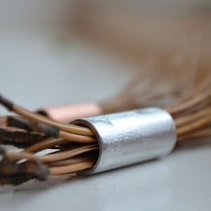 Puede incluir: Un manojo de tallos de plantas marrones secos con una tapa de metal plateado en el extremo.