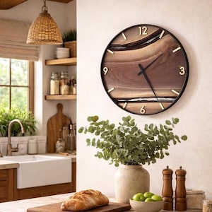 Peut inclure: Une horloge murale ronde avec un cadran en bois foncé et un cadre en métal noir. L'horloge comporte des chiffres dorés aux positions 12, 3, 6 et 9. L'horloge est fixée sur un mur de couleur claire. L'image montre également une cuisine.