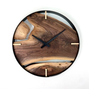 Peut inclure: Une horloge murale ronde en bois avec un cadre en métal noir et des accents dorés. Le cadran de l'horloge est fait d'une tranche de bois naturel avec un motif de grain unique. Les aiguilles de l'horloge sont noires.