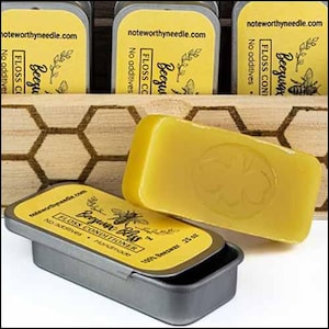 May include: A close-up of beeswax floss conditioner. The image shows a yellow rectangular block of beeswax with a bee imprint, next to an open tin with a yellow label that reads "Beezu Bliss Floss Conditioner". The background includes more tins and a wooden honeycomb pattern.
