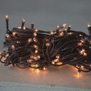 May include: A close-up of a bundle of brown string lights with small, warm white bulbs. The lights are clustered together, creating a cozy and festive atmosphere. Ideal for decorating during the holidays or adding a soft glow to any space.