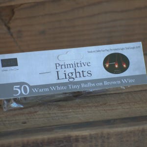 May include: A package of "Primitive Lights" with 50 warm white tiny bulbs on brown wire. The package has a white and gray design with the text "Steady on | Safety Fuse Plug | Pre-tested to Light | Total Length: 10 FT".