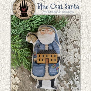 May include: A cross-stitch pattern featuring a Blue Coat Santa holding a house. The Santa figure is dressed in a blue coat with black boots and a white beard. The text "Blue Coat Santa" and "cross stitch chart by Teresa Kogut" are visible.