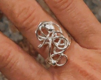 May include: A silver ring with a unique, abstract design. The ring is made of twisted wire and has a delicate, intricate look.