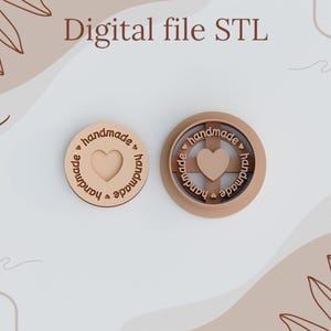 May include: Two wooden round stamps with the word "handmade" and a heart design. The stamps are on a white background with a brown and beige design.