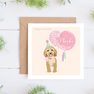 May include: A pink and white birthday card featuring a doodle of a dog wearing a party hat and holding pink balloons. The balloons have confetti and the text "Phoebe" on one of them. The card has the text "Happy Birthday" at the top.