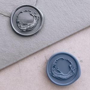 Könnte beinhalten: Zwei Wachssiegel, eines silberfarben und eines blaufarben, mit einem Wellenmuster. Das silberfarbene Siegel befindet sich auf einem grauen Umschlag, während das blaue Siegel auf einer hellrosa Oberfläche liegt. Die Siegel sind rund und weisen ein detailliertes Wellenmuster auf.
