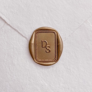 Peut inclure: Un sceau de cire doré avec les initiales "DS" dans un cadre rectangulaire bordé de perles. Le sceau est apposé sur une enveloppe blanche, créant une esthétique classique et élégante.