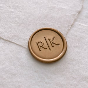 Modern font monogram self-adhesive wax seal in gold on white handmade paper envelope, side angle