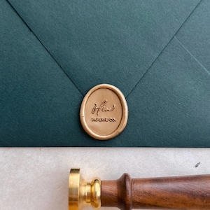 custom brand logo gold wax seal on a dark green envelope next to a brass wax stamp with a walnut wooden handle