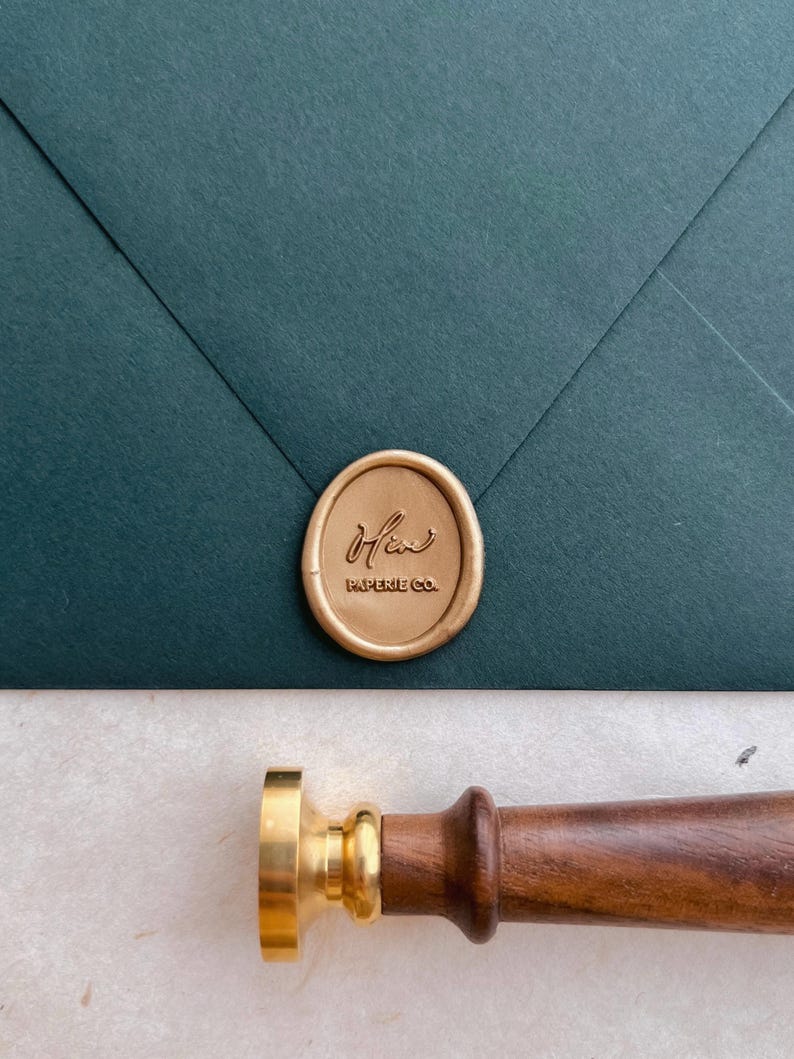 custom brand logo gold wax seal on a dark green envelope next to a brass wax stamp with a walnut wooden handle
