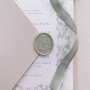 Light metallic green vintage crest monogram oval wax seal on a wedding invitation card and beige envelope