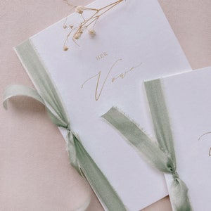 A set of 2 white vow books gold foil printed with His Vows and Her Vows in calligraphy script, tied in sage green silk ribbon