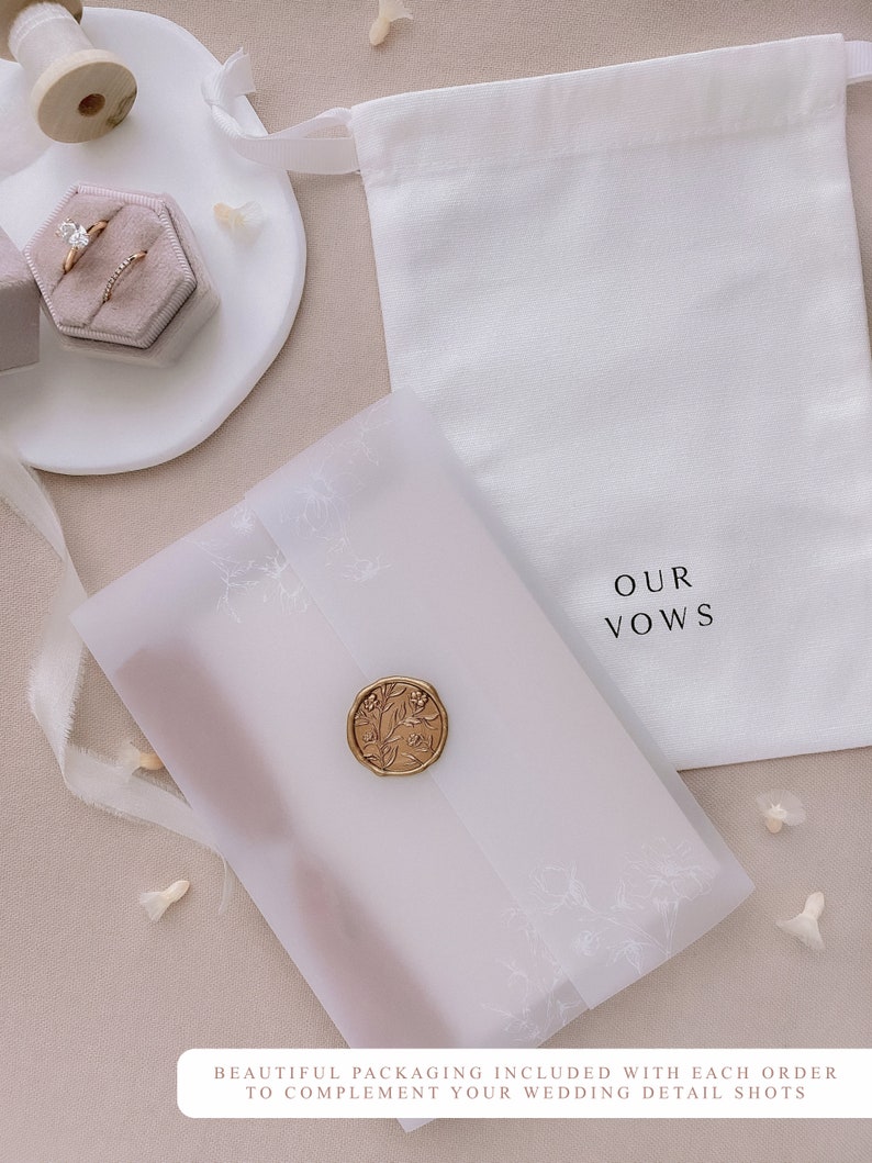 Vow books packed inside white floral vellum jacket, adorned with a gold wax seal, placed next to a white keepsake linen pouch