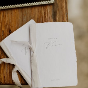 Set of 2 white handmade paper vow books printed with personalized names and date, tied in off-white silk ribbons
