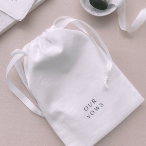 White keepsake pouch in white drawstring with OUR VOWS printed on it in black ink