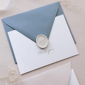 gold foil embossed white thank you card with dusty blue envelope and white wax seal