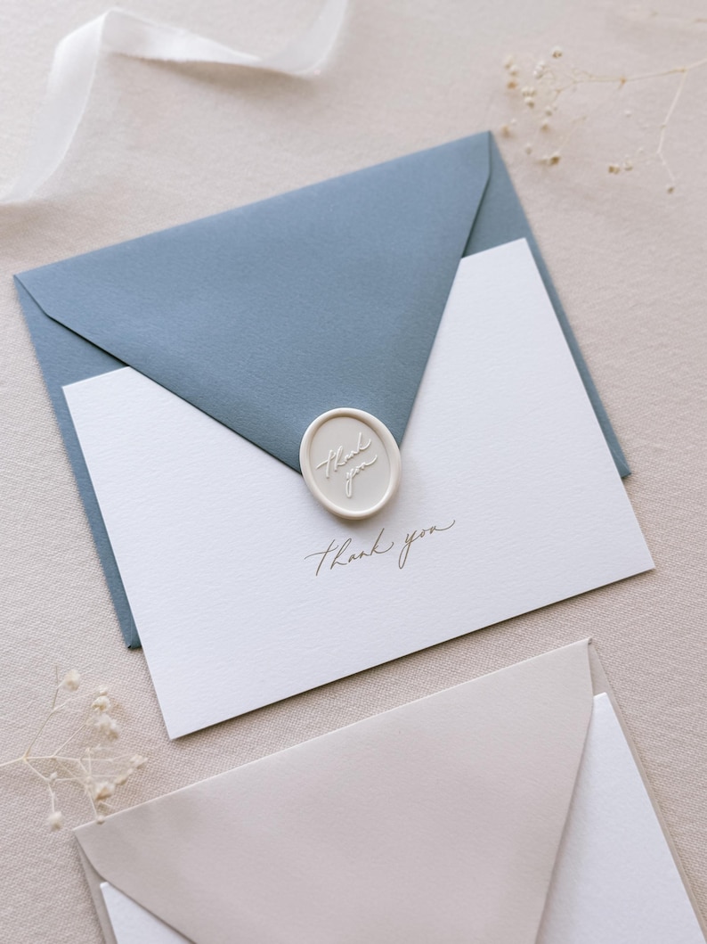 gold foil embossed white thank you card with dusty blue envelope and white wax seal