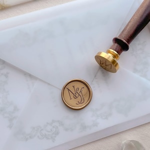 Custom monogram gold wax seal on a vellum wedding invitation envelope and a wax seal stamp next to it
