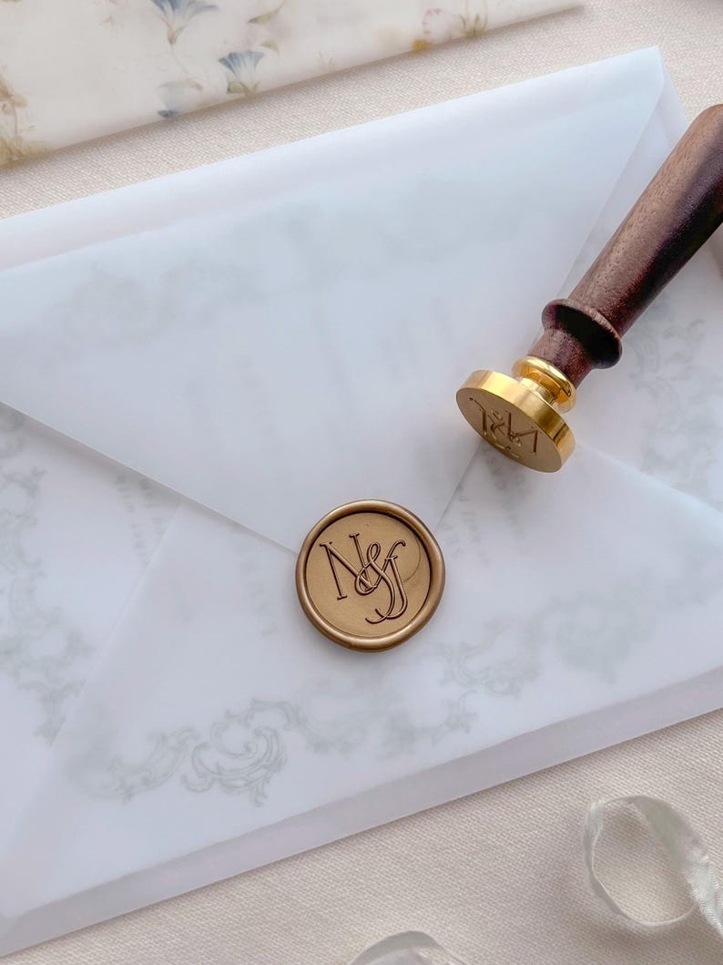 Custom monogram gold wax seal on a vellum wedding invitation envelope and a wax seal stamp next to it