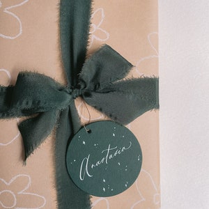 Gift wrapped in Christmas silk ribbon in dark green adorned with round gift tag in deep green