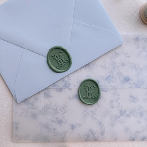 Green vintage interlocked monogram wax seals on blue envelope and blue floral print vellum jacket