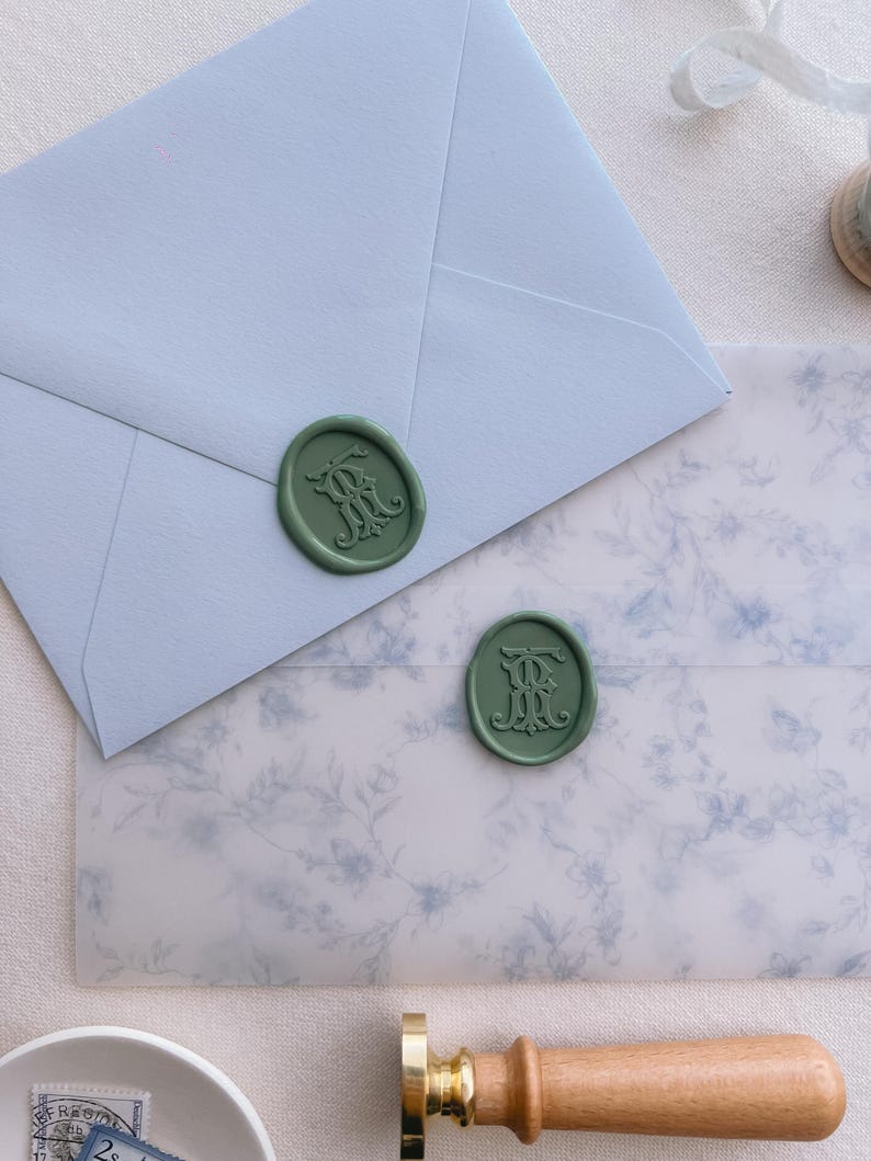 Green vintage interlocked monogram wax seals on blue envelope and blue floral print vellum jacket