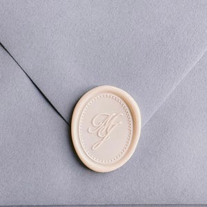 off-white oval monogram wax seal on dusty blue envelope