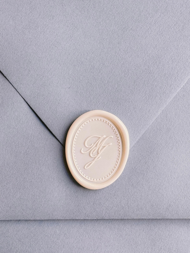 off-white oval monogram wax seal on dusty blue envelope