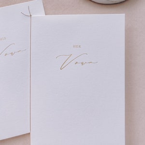 A set of 2 white vow books gold foil printed with His Vows and Her Vows in calligraphy script, tied in brown twine