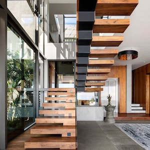 Może przedstawiać: Nowoczesne schody z drewnianymi stopniami i czarną metalową balustradą. Schody znajdują się w nowoczesnym domu z dużymi oknami i widokiem na zewnątrz.