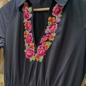 May include: Black short-sleeved dress with a V-neck and embroidered floral detail around the neckline. The dress has a gathered waist and is made by Zara.