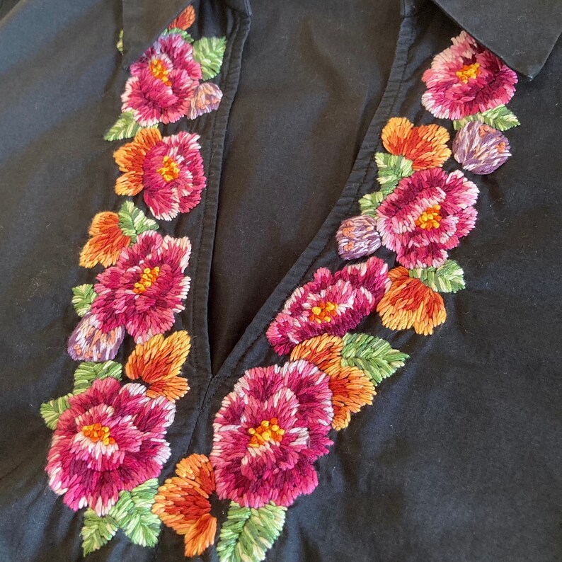 May include: Black cotton shirt with a V-neck and embroidered floral design around the neckline. The flowers are pink, red, and orange.