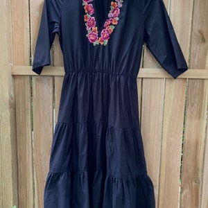 May include: A black tiered midi dress with a collared neckline and embroidered floral detail around the neckline. The dress has a v-neck and 3/4 sleeves.