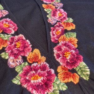 May include: Black dress with a deep V-neckline and embroidered floral details in shades of pink, orange, and green.