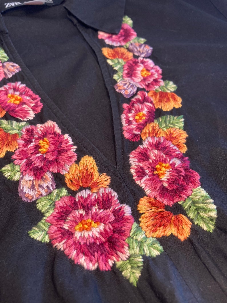 May include: Black dress with a deep V-neckline and embroidered floral details in shades of pink, orange, and green.