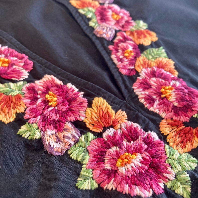 May include: Black fabric with embroidered pink, red, and orange flowers. The flowers are arranged in a symmetrical pattern along the edges of the fabric.