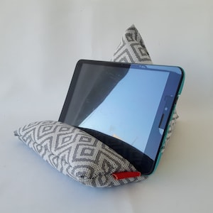 Puede incluir: Un soporte de almohada de tela con estampado gris y blanco para una tableta. El soporte está hecho de tela y tiene una cremallera roja. La tableta no está incluida.