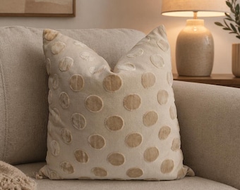 Cojín decorativo beige con tejido texturizado y acabado elegante.