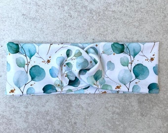 May include: A white headband with a knotted design features a watercolor print of eucalyptus leaves in shades of blue and green with gold accents.