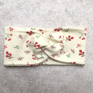 Könnte beinhalten: Ein weißes Stirnband mit einem Blumenmuster in Rot- und Grüntönen. Das Stirnband ist zu einem Knoten gedreht.